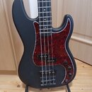 Čtyřstrunná basová kytara s matně černým povrchem korpusu a hmatníkem. Nástroj má červeně vzorovaný pickguard, dva snímače a tři ovládací knoflíky. K…