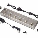 Stříbrný kovový napájecí adaptér s nápisem Harley Benton a STOMPCONTROL-4 ISO. Zařízení má šest kovových přepínačů a několik konektorů na horní stran…
