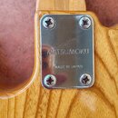 Detail zadní strany krku dřevěného nástroje s kovým šildkem připevněným čtyřmi šrouby. Na šildku je vyryto MATSUMOKU a pod tím nápis MADE IN JAPAN. P…