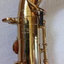 Detail zlatého saxofonu z mosazi. Na trubici je vyryto označení ATS 63 a pod ním nápis CZECH REPUBLIC. Povrch nástroje vykazuje drobné škrábance a zn…
