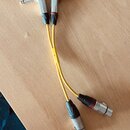 Dva žluté audio kabely s konektory 6,3mm jack na jedné straně a XLR na druhé straně. Konektory jsou kovové s černými gumovými chrániči. Na kabelech n…