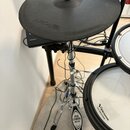 Fotografie zachycuje část elektronické bicí soupravy. V horní části je černý gumový činel s logem Roland. V pravé části jsou vidět dva bílé bubny s n…