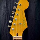 Zadní strana hlavy elektrické kytary v žluté barvě s viditnou strukturou dřeva. Na zadní straně je svisle umístěno logo Squier a nápis STRATOCASTER®.…