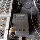 Černý síťový adaptér značky PHONIC s bílým štítkem. Na štítku je text: AC ADAPTOR, P/N: 353-21904-000-0, INPUT: 230V AC 50Hz, OUTPUT: 16.8Vx2 AC 1A a…