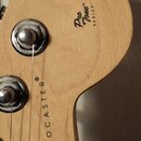 Detail hlavy elektrické kytary z přírodního dřeva. Na povrchu jsou nápisy Pro Tone™ SERIES a STRATOCASTER®. V dolní části je viditelné logo Fender. J…