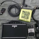 Sada vybavení obsahuje černý kytarový kombo zesilovač s bílým logem BOSS a symbolem katany. Vedle něj je šedý pedál s nápisy NOISE REDUCER NR300 a lo…