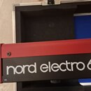 Detailní pohled na červený digitální klavír s černým panelem. Na panelu je bílý nápis nord electro 6 D a v levém dolním rohu malý nápis v1.1. Povrch…