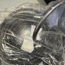 Černý kabel svlnutý do klubíčku, který je zabalen v průhledném plastovém sáčku. Uvnitř sáčků jsou vidět bílé papírové sáčkky s nápisy SILICA GEL. Na…