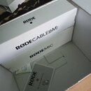 Fotografie zachycuje bílé papírové krabice a příslušenství. Na horní krabici je logo RØDE MICROPHONES a nápis RØDECABLE(6M) s part numberem Part No.…