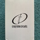 Bílá papírová krabice s černým potiskem. Uprostřed je logo znázornující stylizované písmeno „t“ obklopené elipsou a pod ním nápis „crazy tube circuit…