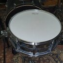 Fotografie zachycuje bílý buben s chromovaným obručováním a kování. Na blaně je nápis „Ludwig Drums“ a pod ním slovo „HEAVY“. Na spodní části korpusu…