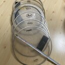 Sada šesti průhledných bubnových blan s kovovými obručemi, položených na dřevěné podlaze. Na blanách jsou vidět nápisy a loga značek EVANS, REMO (mod…