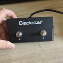Černý obdélníkový box s nápisem Blackstar. Na přední straně jsou dvě kovová tlačítka označená písmeny A a B. Z horní části zařízení vychází černý kab…