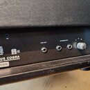 Zadní panel kytarového komba s černým povrchem. Jsou zde viditelné konektory s nápisy LINE OUT a SPEAKER OUT, symbol CE a logo ve tvaru písmene Z. V…