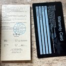 Fotografie zobrazuje dva dokumenty: záruční list v čínštině a černou plastovou kartu s nápisem Warranty Card. Na bílém papíře je u políčka Model uved…
