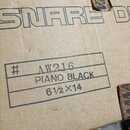 Fotografie zachycuje detail hnědé kartonové krabice. V horní části je vidět nápis SNARE D a v tabulce jsou ručně zapsány údaje # AW216, PIANO BLACK a…