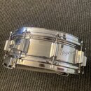 Kovový snare drum s chromovaným povrchem. Na boku je viditelné logo TAMA. Nástroj vykazuje známky používání v podobě drobných škrábanců na povrchu.