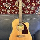 Akustická kytara s vyřezem v těle, přírodní dřevěnou barvou a hnědým hmatníkem. Na hlavě je bílý nápis Epiphone a na štítku uvnitř otvoru zvukové dír…