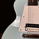 Detail elektrické kytary v světle modré barvě s bílým pickguardem. Nástroj má hnedý hmatník a jeden snímač typu humbucker s bílými pólky. Na povrchu…