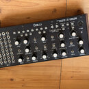 Černý analogový syntetizátor Moog MOTHER-32 s dřevěnými bočními panely. Na horním panelu jsou umístěny početné bílé otočné knoflíky, tlačítka a zapoj…