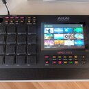 Černý sampler MPC s 16 gumovými pady v horní části. Na přístroji je vidět nápis MPC LIVE II a logo AKAI PROFESSIONAL. Zařízení má barevně podświetlen…