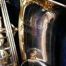 Detail zlatého saxofonu v modrém pouzdře. Na korunu nástroje je vyryt nápis Elkhart SERIES II. Povrch je lesklý s viditelnými odlesky a drobnými neči…
