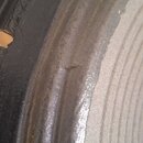 Detailní záběr na okraj černého reproduktoru. Gumový nebo pěnový подвеs vykazuje v horní části viditelné opotřebení ve formě trhliny. Žádné značky an…
