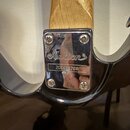 Detail spojení krku a těla kytary s chromovaným krytem. Na krytu je vyryto logo Jackson a pod ním je nalepený štítek se sériovým číslem 200600766. Po…