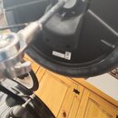 Fotografie zachycuje spodní stranu černého elektronického činely a část černého bubnu. Na spodní straně činely je vyražen nápis Roland a viditelná bí…