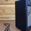 Černý kytarový kombozesilovač s texturovaným povrchem a šedou přední síťovkou. Na pravé straně je vidět bílé logo Fender. Vedle zesilovače leží černý…