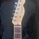 Hlava a hриф elektrické kytary v přírodním dřevě s hnědým hmatníkem. Na hlavě je černé logo Fender, nápis TELECASTER® a menší text MADE IN U.S.A. Kyt…