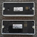 Dvě obdélníková elektronická zařízení v bílých plastových krytech s černým spodním panelem. Horní jednotka má štítek s nápisy EMG-707, MADE IN USA 38…