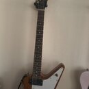 Elektrická kytara s hnědým dřevěným korpusem ve tvaru Explorer a bílým pickguardem. Na hlavě hmatníku je bílý nápis Epiphone. Nástroj má dva humbucke…