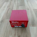 Červený kovový box s nápisem Weber. Na přední straně jsou přepínače označené jako IMPEDANCE (8Ω, 16Ω, 4Ω), NORMAL a TREBLE (6db, 0db, 3db) oraz otočn…