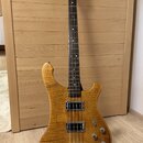 Elektrická basová kytara s přírodním dřevěným povrchem a výraznou kresbou zrna. Nástroj má dva snímače typu humbucker, tři ovládací knoflíky a chromo…