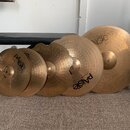 Sada pěti mosazných činelů různých velikostí. Na několika činelech je vidět logo Paiste a označení Zildjian 2002. Povrchy činelů vykazují známky použ…