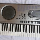 Stříbrný elektronický klavír značky CASIO s nápisem MUSICAL INFORMATION SYSTEM. Nástroj má v levé části dva menší a jeden velký integrovaný reprodukt…