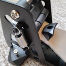 Detailní pohled na černý kovový mechanismus pedálu. Je vidět pružina, klouby s vložkami a část kovové šlapky. Na povrchu jsou vidět drobné prachové č…