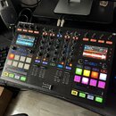 Černý DJ kontrolér s nápisem TRAKTOR KONTROL S5. Zařízení obsahuje dva displeje, zahlreichetočítka, posuvníky a podsvícené čtvercové pady v různých b…