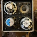 Kvadratický reproduktorový box v hliníkovém flightcase s černým dnem a čtyřmi kolečky. Box obsahuje čtyři reproduktory, z nichž dva mají viditelné bí…