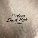 Detailní záběr na povrch činelu s kovaným zpracováním. Uprostřed je černý nápis Custom Dark Ride a pod ním rozměr 22"/56cm. Povrch vykazuje drobné zn…