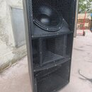 Černý reproduktorový systém v bedně s kovovými ochrannými mřížkami. Sestává ze tří sekcí, přičemž v horní části je viditelný velký kruhový reprodukto…