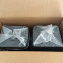 V kartonové krabici jsou dva černé, kostkovité předměty. Oba jsou zabaleny v průhledné plastové fólii. Na předmětech nejsou vidět žádné značky ani ná…