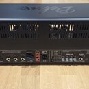 Zadní strana černého kytarového komba s nápisem Deluxe na horní části. Na spodním panelu jsou viditelné konektory a ovládací prvky s popisky MIDI, FX…
