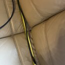 Modrý kabel položený na béžovém koženém povrchu vedle žlutého krejčovského metru. Na kabelu nejsou viditelné žádné značky ani nápisy. Konec kabelu za…