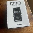 Bílá krabice s nápisem DITTO STEREO LOOPER a logem tc electronic. Na krabici je zobrazen černý kytarový pedál s nápisy LOOP LEVEL, STORE, RECORD/PLAY…