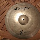 Kovový činel v přirozené zlatavé barvě s viditelným rýhováním. V horní části je černý nápis „alchemy cymbals“. Ve spodní části je černý kříž a vedle…