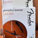Dvě bílé krabičky s tóny pro akustickou kytaru. Na obalích je uveden nápis phosphor bronze, značka Fender a slogan MAKE HISTORY™. Je zde specifikace…