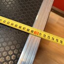 Detailní záběr na roh černého transportního kufru s povrchem ve tvaru včelího plástre. Kufr má hliníkové hrany a rohové zakončení. Přes hranu je přil…