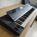 Černý elektronický klávesový nástroj s bílými a černými klávesami. Na ovládacím panelu je nápis YAMAHA DSR-2000. Nástroj obsahuje řadu barevných tlač…